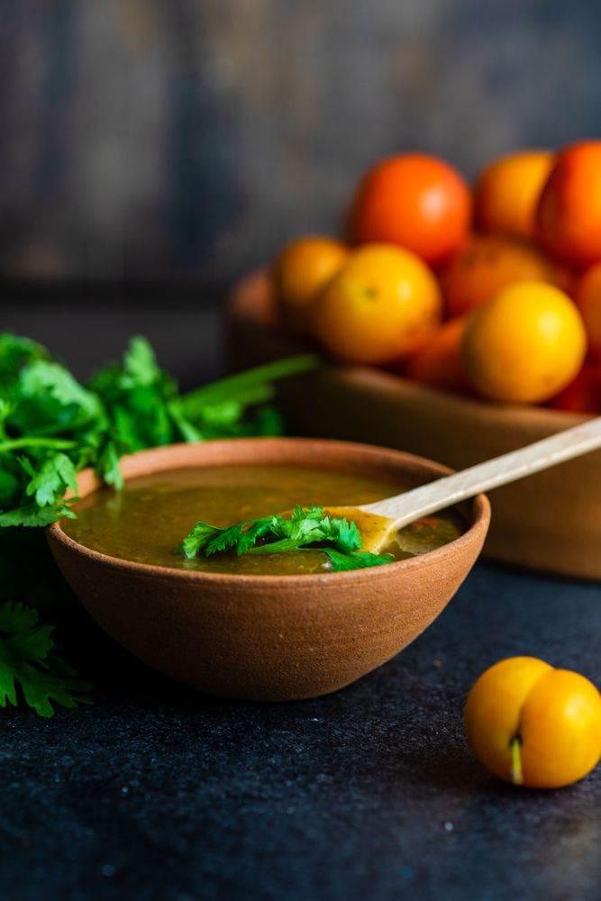 Bowl of plums and fresh parsley with Georgian Tkemali Sauce on dark table