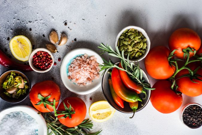 Top view of tomatoes, Himalayan salt, red peppercorns, lemon, garlic & herbs on counter with copy space