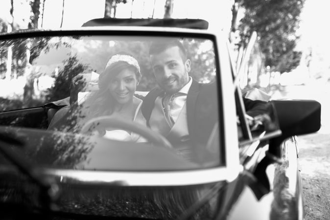 Newlyweds driving off together after ceremony in vintage car