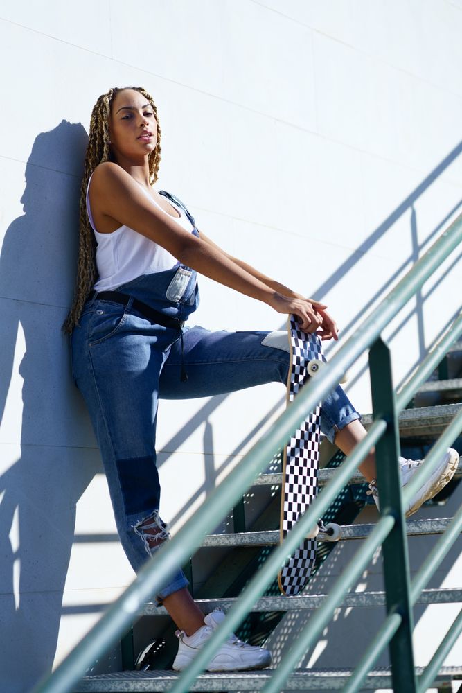 Side view of female standing on green stairs with skateboard