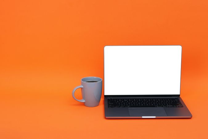 Laptop with mockup screen with cup of coffee or tea in orange studio shoot with copy space