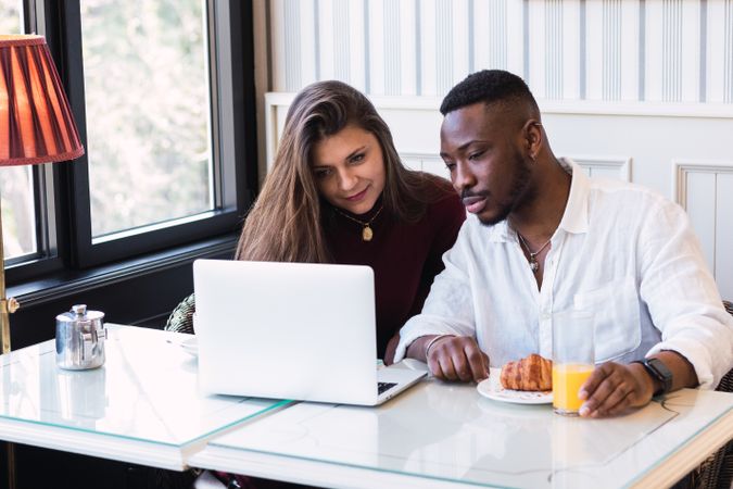 Cheerful Black couple using laptop during breakfast at home