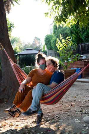 Young couple sitting in hammock with masks on