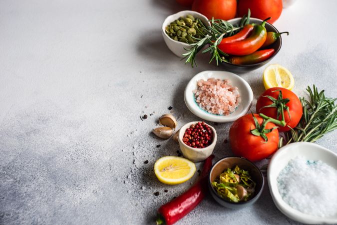 Vine tomatoes, Himalayan salt, red peppercorns, lemon, garlic & herbs on counter with copy space