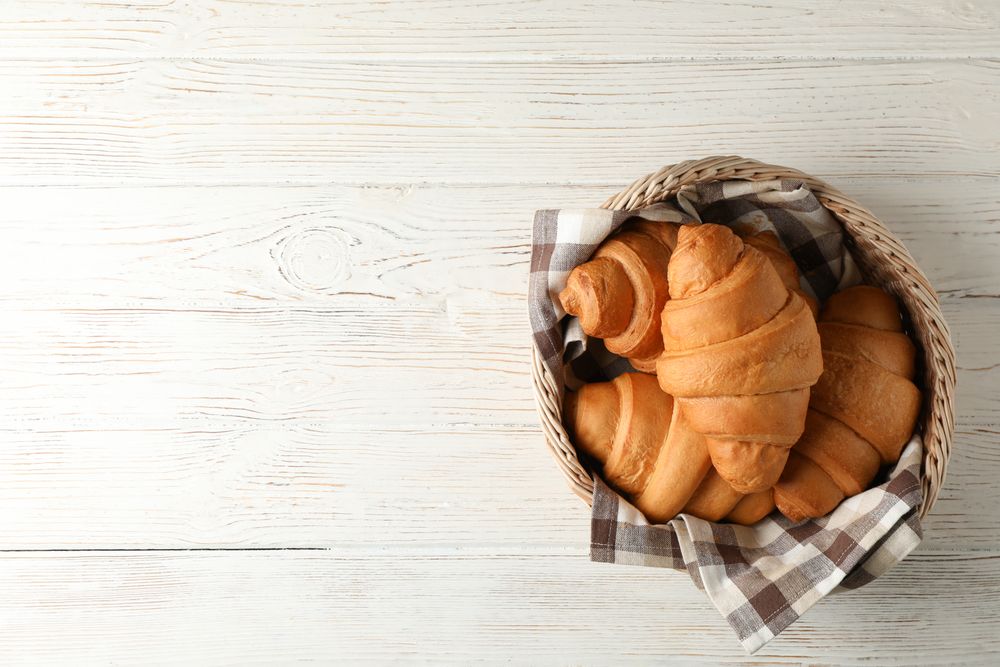 Top view of wicker basket with croissants on wooden table, copy space