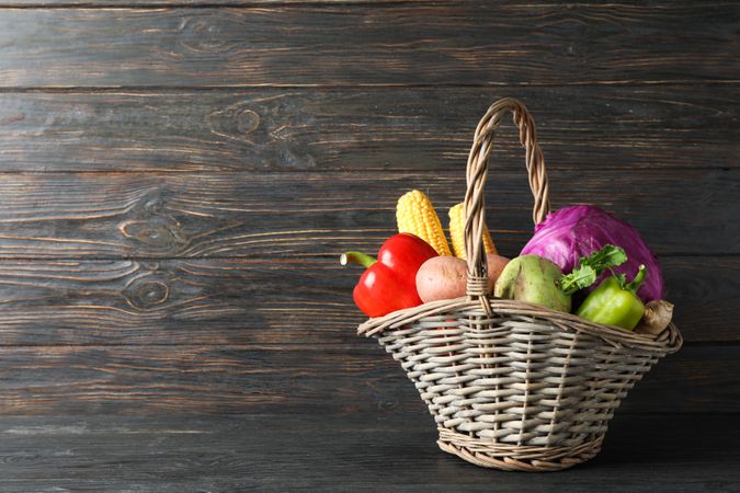 Wicker basket with vegetables on wooden background, copy space