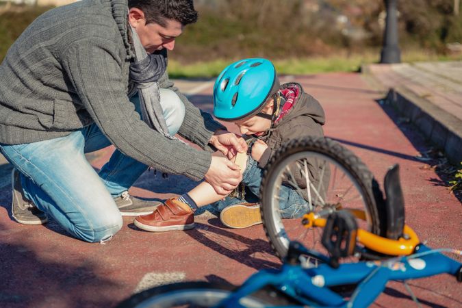 Father tending son's knee after falling off his bike