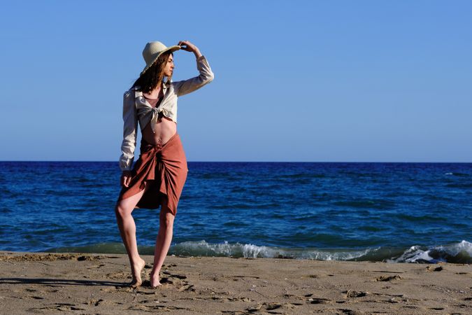 A fashion model with a hat at the beach before sunset