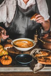 Woman in apron with spoon and bread eating soup in cozy kitchen