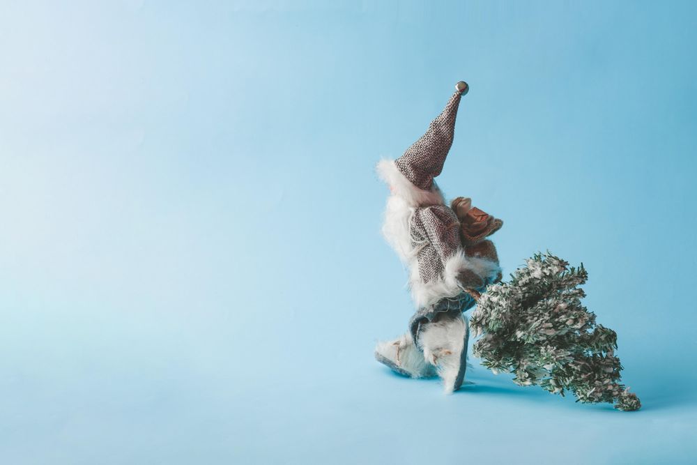 Santa Claus dressed in gray pulling Christmas tree with bright blue background