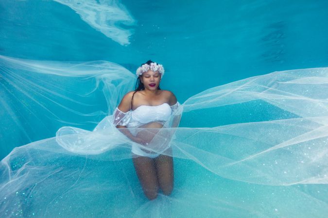 Pregnant woman in wreath and dress underwater