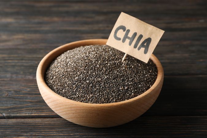 Wooden bowl and word Chia on wood background, copy space