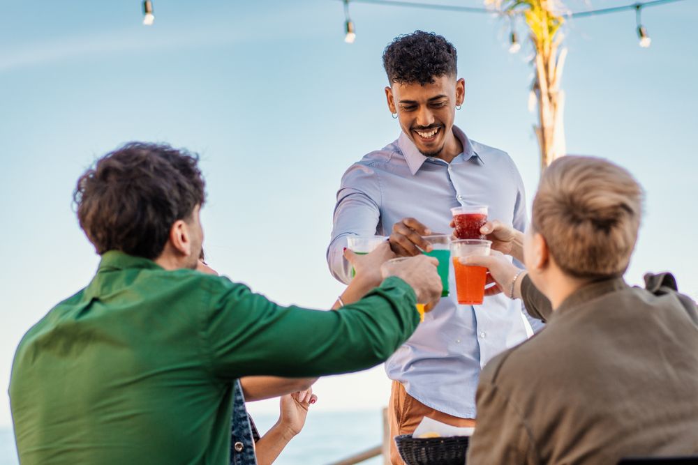 Multicultural friends toasting with colorful drinks at beachside celebration