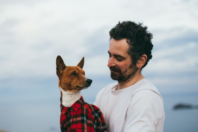 Sleepy dog wearing plaid shirt on a cliff with male owner