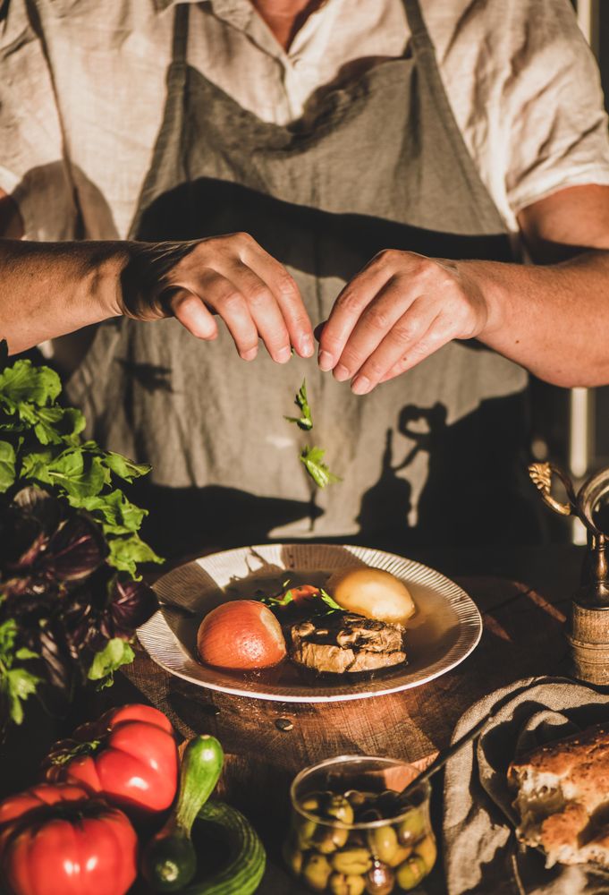 Woman in gray apron putting herbs on stew