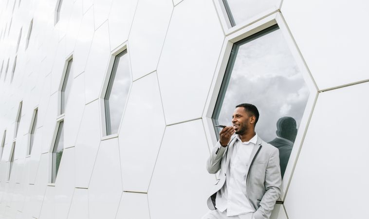 Elegant Black man talking smartphone leaning on geometrical wall