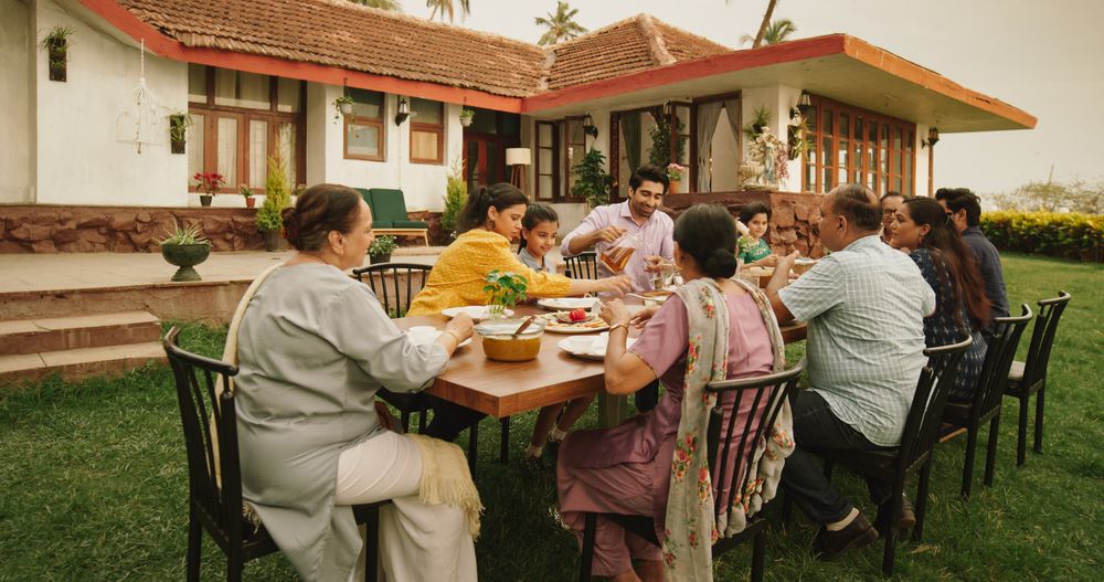 Happy Extended Indian Family Eating Together Outdoors in House Backyard.