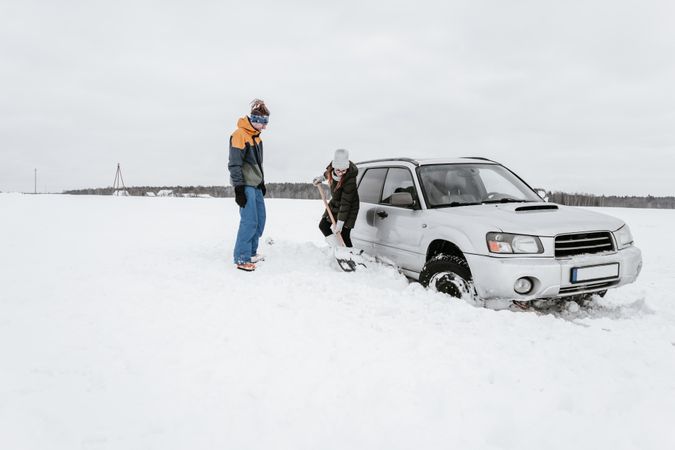Woman with shovel near man and car on snow field