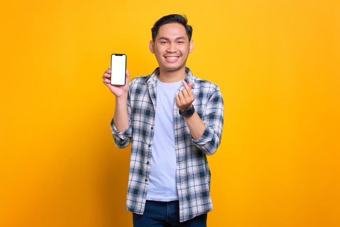 Asian male showing blank screen of smart phone making heart sign with his hand
