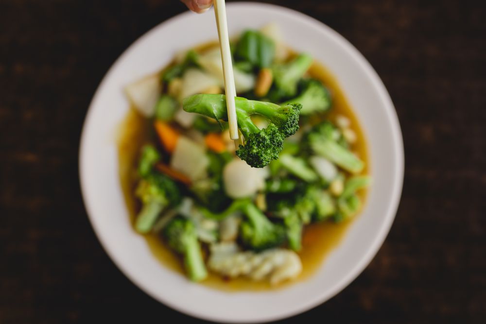 Hand holding broccoli with chopsticks over vegetarian soup