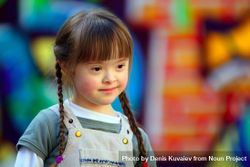 Girl with Down syndrome and braided hair against a colorful background beNxp0