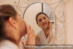 Female in mirror applying cream on her face 5RV1KD
