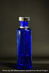 Blue perfume bottle with droplets in grey studio with copy space 47meBP