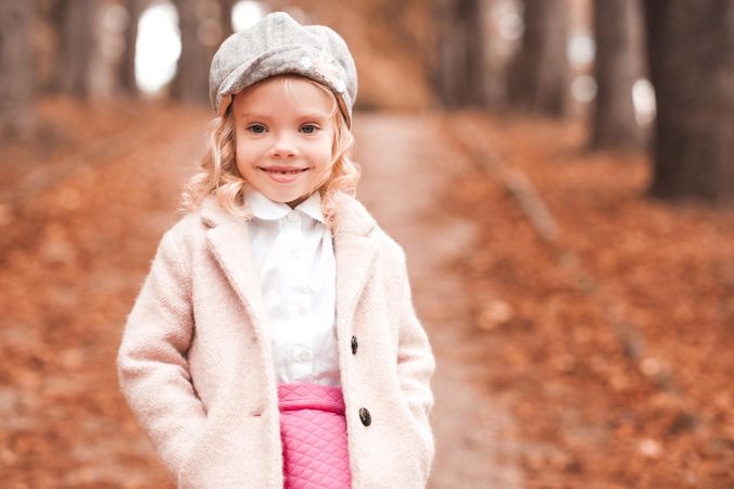 Young girl wearing pink jacket standing on fallen autumn tree leaves