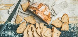 Homemade loaf, with slices arranged in line with serrated knife, on wooden board, wide composition