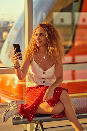 Smiling woman sitting on metal bench with earphones and smartphone