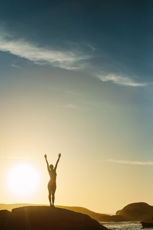 Silhouette of a woman standing on the beach with her hands raised