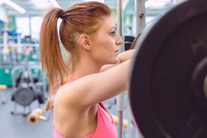 Serious woman leaning on barbell in gym