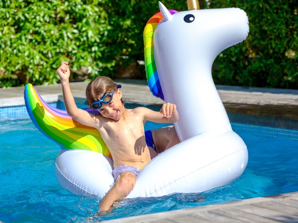 Positive child sitting on inflatable unicorn in outdoor swimming