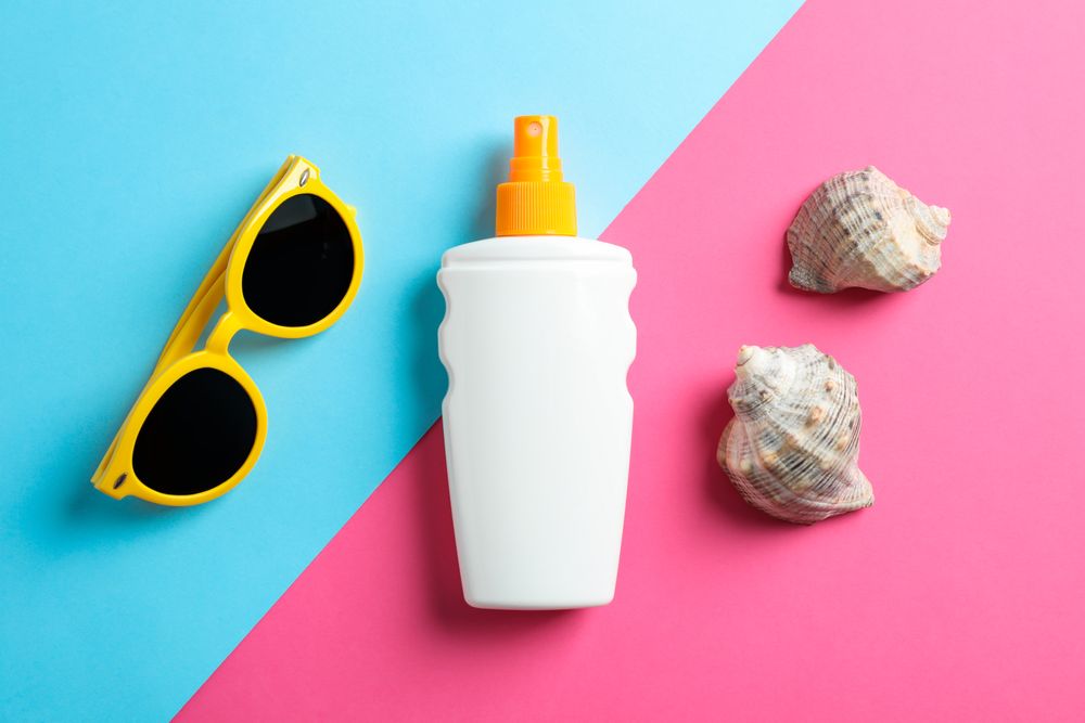 Flat lay composition with sunglasses, sunscreen pray and seashell on two tone background, top view, closeup. Summer vacation backdrop