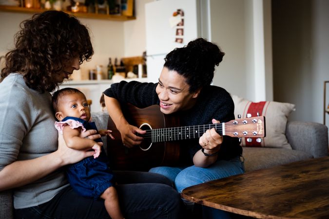 Mother playing acoustic guitar for baby and partner