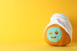Pumpkin with facial mask and towel on yellow background, copy space