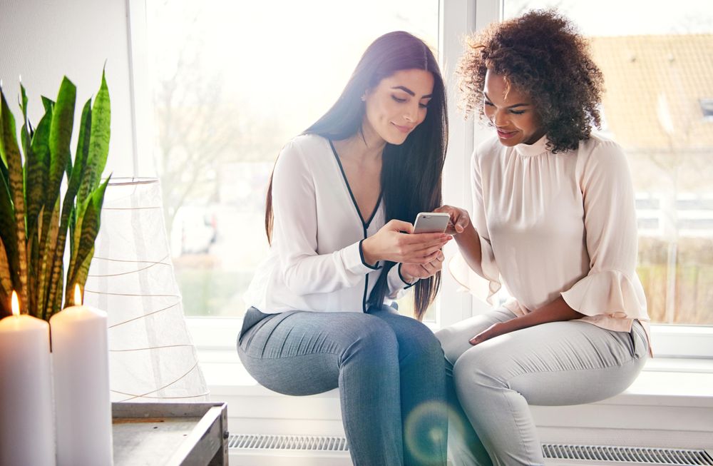 Two woman looking at a smartphone together by the window