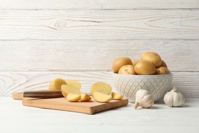 Side view of bowl full of potatoes on kitchen counter with garlic and cutting board