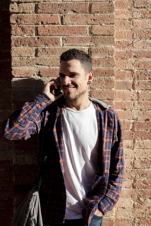 Young man leaning on a brick wall talking on his smartphone