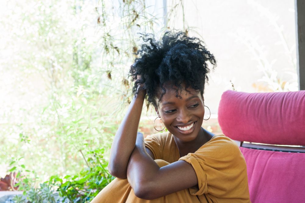 Woman with curly bun and bright smile sitting under covered patio area looking away