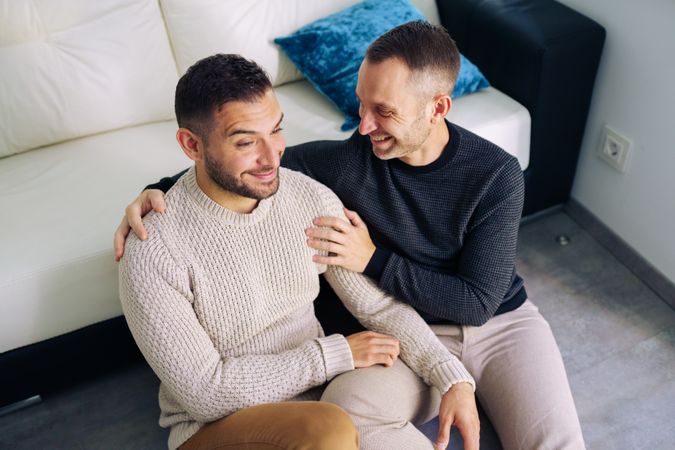 Cute male couple sitting on floor and laughing together at home