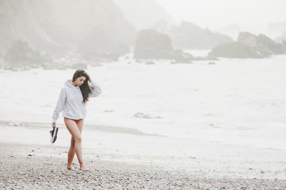 Woman walking on shore near stones and water