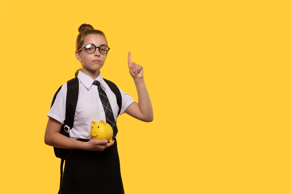 Schoolgirl holds piggy bank while raising finger.