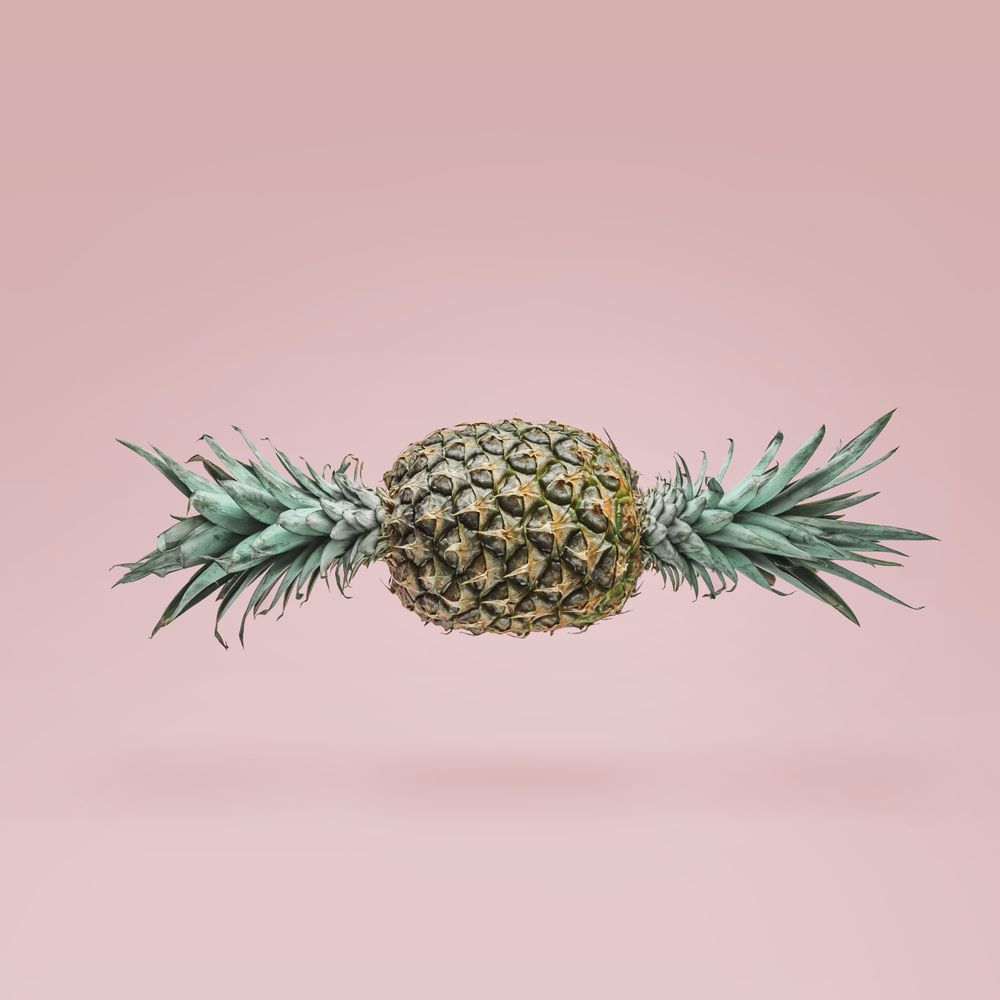 Pineapple in shape of candy with green top on both ends on blush background