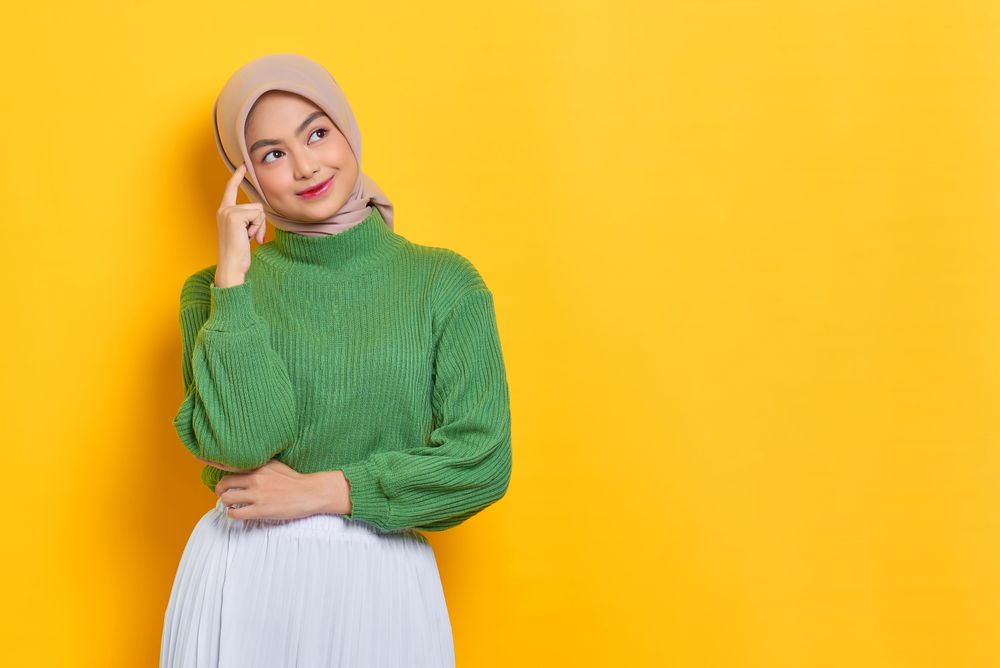 Woman in headscarf thinking with hand to head with yellow copy space