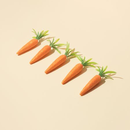 Row of carrots on pastel yellow background