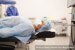 Woman in hair net and facemask lying down pre-surgery 5azZ84