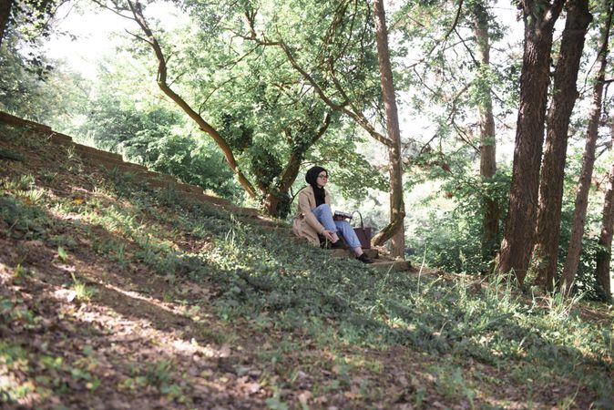 Middle Eastern woman sitting on grassy hill with book