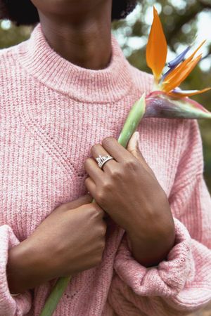 Close-up shot of woman in pink sweater holding flower to her chest
