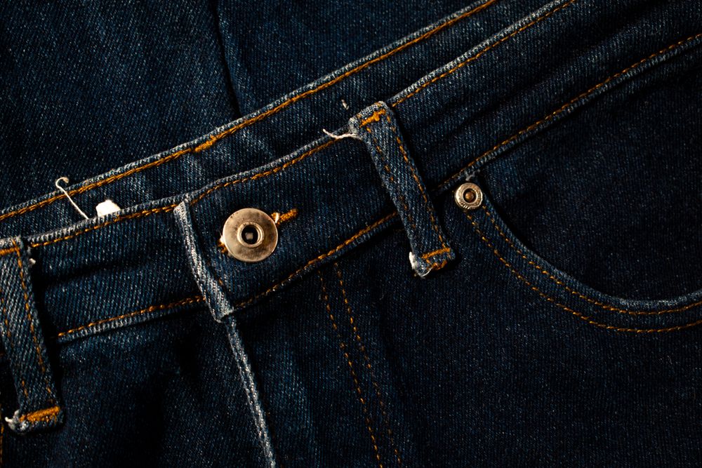 Close up gold and shiny button navy blue jeans fabric background texture.